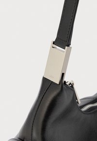 Angolo di una borsa in pelle nera con fibbia rettangolare in metallo argentato e zip visibile su sfondo bianco.