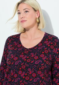 Schwarzes Oberteil mit V-Ausschnitt, verziert mit einem bunten Paisley- und Blumenmuster in Rot, Lila und Orange auf einem glatten Stoff.