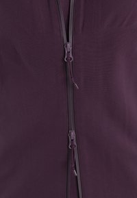 Fioletowa kurtka zapinana na zamek, o gładkiej, matowej teksturze, z kontrastowym ciemniejszym zamkiem i uchwytem do łatwego otwierania.