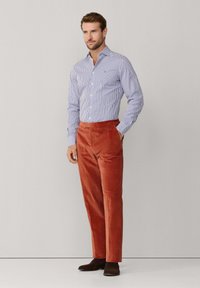 Striped blue and white button-up shirt, paired with rust-colored corduroy trousers and brown shoes. Simple design, tailored fit.
