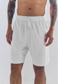 Pantalones cortos deportivos de color gris claro con cintura elástica, detalle de cordón y tela suave, que terminan por encima de la rodilla.