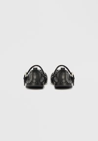 Čierne kožené sandále s pásikom na päte, s okrúhlymi výrezmi, plochou podrážkou a detailom bielych stehov pozdĺž okrajov.