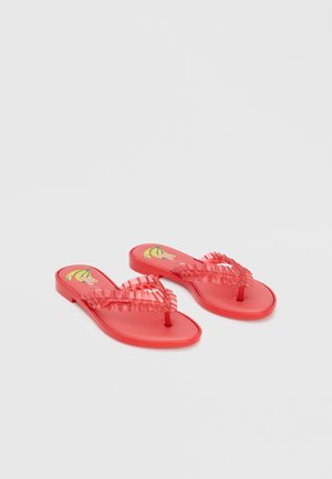 Sandales plates rouges avec brides froncées et motif banane sur la semelle intérieure, affichées sur un fond clair uni.