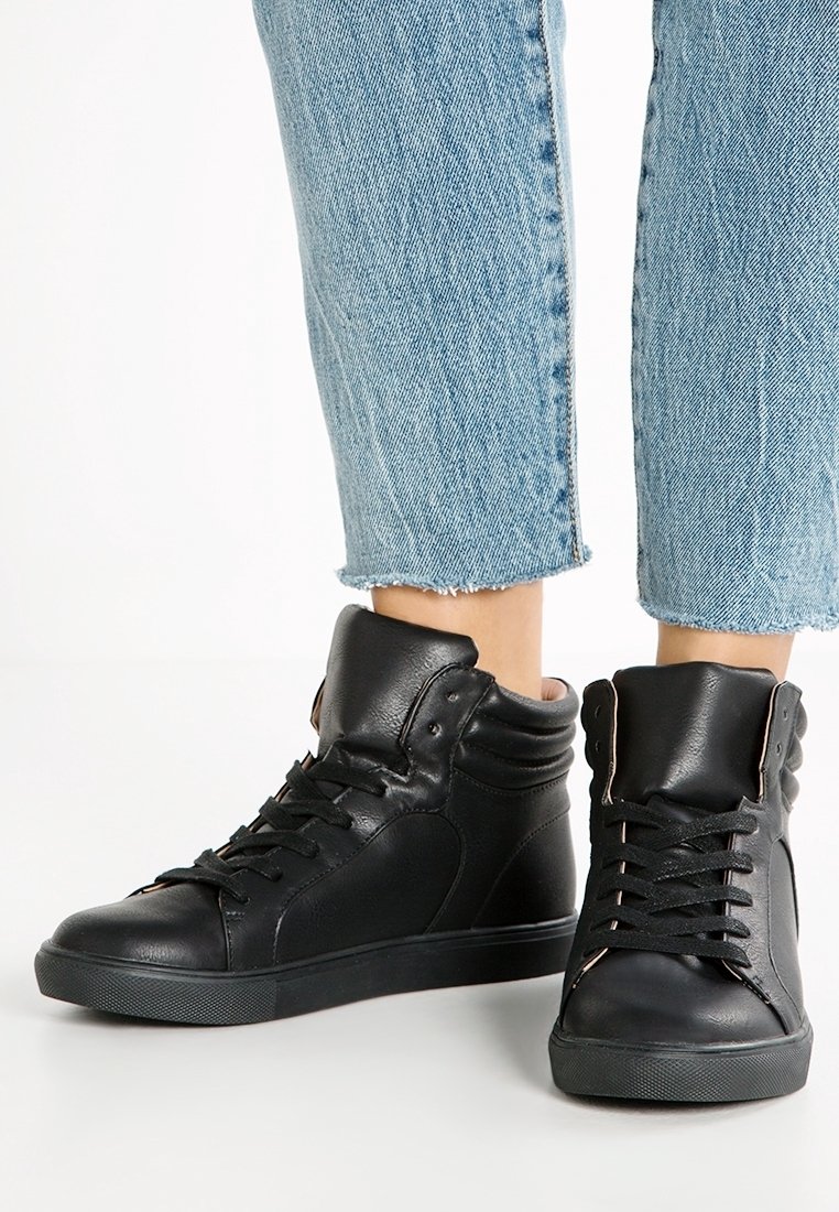 Černé kožené vysoké tenisky mají zaoblenou špičku, šněrování a texturované detaily. Silná gumová podešev zajišťuje přilnavost a odolnost.