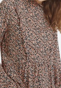 Blommig klänning med svart bakgrund och små rosa och vita blommor, volangkrage och långa ärmar. Mjuk, lätt stoff.