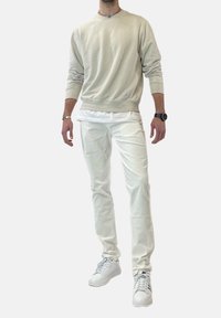 Světle béžová mikina s žebrovanými manžetami a lemem, spárovaná s bílými slim-fit kalhotami a bílými teniskami. Ležérní, minimalistický design.