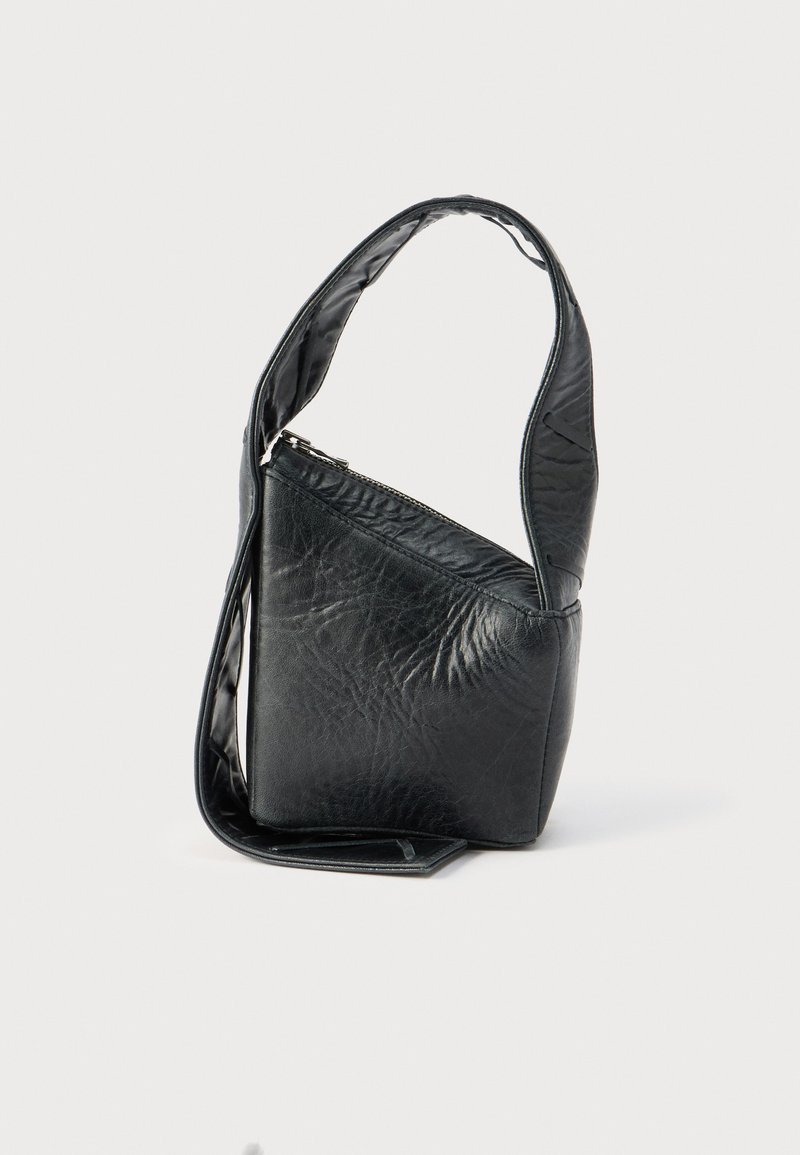 Μικρό μαύρο δερμάτινο τσαντάκι με ένα φαρδύ λουράκι και φερμουάρ στην κορυφή, όρθιο σε απλό λευκό φόντο.