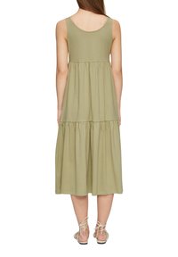 Robe sans manches à volants de couleur vert olive, avec un col rond et une taille froncée. Fabriquée en tissu doux, s'arrêtant mi-mollet, accompagnée de sandales légères.