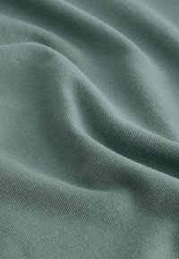 Mjuk grön textil med en slät yta, med subtila stickmönster och mjuka draperingar, lämplig för kläder eller möbelklädsel.