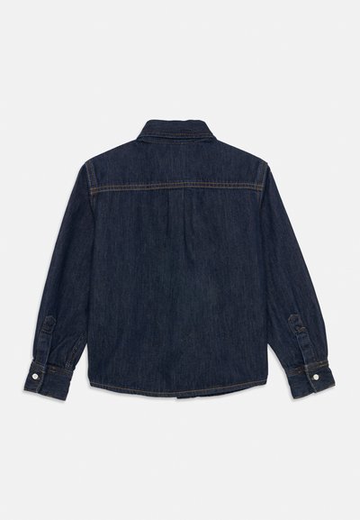 Chemise en denim bleu foncé avec un col, des poignets à boutons et une pièce d'épaules. Comprend de grands plis au dos pour un confort optimal et des coutures subtiles.
