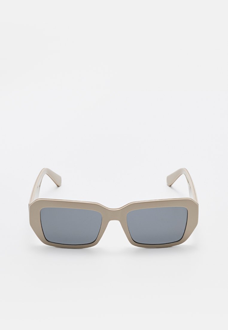 Beżowe prostokątne okulary przeciwsłoneczne z grubymi oprawkami i ciemnoszarymi soczewkami, przedstawione z przodu na białym tle.