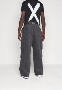 Černé tričko s velkým bílým znakem „X“ na zádech, doplněné tmavě šedými cargo kalhotami s bočními kapsami a elastickým pasem.