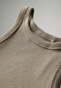 Canottiera ribbed beige con scollatura rotonda e spalline sottili. Presenta cuciture delicate lungo i bordi per una finitura pulita.