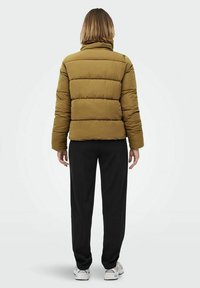 Khaki kurtka puchowa z poziomym przeszyciem, wysokim kołnierzem i elastycznymi mankietami, w połączeniu z czarnymi spodniami i białymi sneakersami, widok z tyłu.