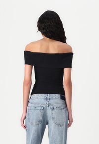 Čierny off-shoulder top s priliehavým strihom, v kombinácii so svetlomodrými džínsy s vysokým pásom, ktoré majú vyblednutú textúru a zadné vrecká.