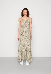 Langes, florales Kleid in hellgrün mit V-Ausschnitt, dünnen Trägern und einem fließenden Saum. Kombiniert mit weißen Schuhen. Mit kleinen, zarten Mustern versehen.