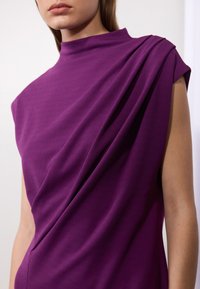Violetti hihaton paita korkealla kaula-aukolla, valmistettu pehmeästä kankaasta. Etupuolella on drapeerattu yksityiskohta ja rakenteellinen olkapäädesign.