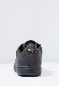 Baskets en cuir noir à finition texturée, avec un logo Puma doré sur le talon et une semelle en caoutchouc avec marquage.