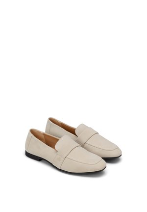 Een paar beige instap loafers met afgeronde neuzen, lage zwarte hakken en een brede band over het bovenwerk, afgebeeld op een witte achtergrond.