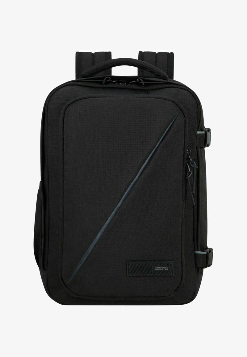 Zaino nero con esterno testurizzato, forma sottile, manico superiore, spallacci imbottiti e una zip diagonale come dettaglio. Presenta una patch con il logo.