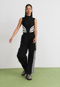 Svart bodysuit med hvite buede detaljer, kombinert med svarte baggy bukser med hvite striper på sidene og sko med sebra-mønster.