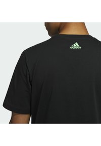 Schwarzes T-Shirt mit kurzen Ärmeln aus leichtem Stoff, auf der Rückseite mit einem grünen Adidas-Logo. Schlichtes Design mit rundem Ausschnitt.
