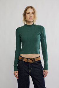 Grønn ribbestrikket kort genser med lange ermer og høy hals, kombinert med mørkeblå denimjeans og et lyst belte med dekorativ spenne.