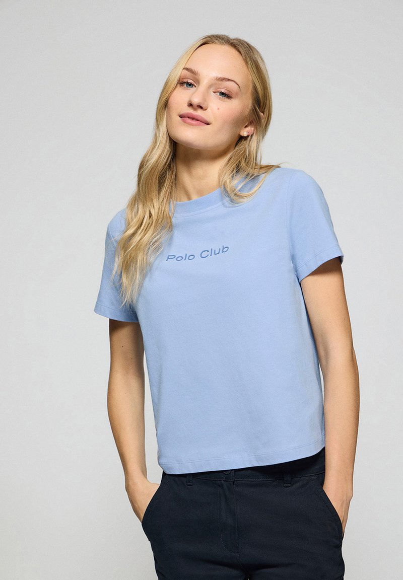 T-shirt en coton bleu clair à manches courtes et col rond, avec "Polo Club" brodé en bleu plus foncé.