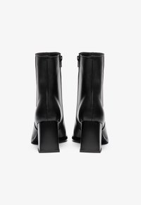 Sorte lær ankle boots med en firkantet, kraftig hæl; har en glat tekstur og stikninger langs bagsiden og siderne.