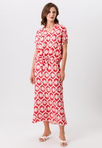 Robe à motifs rouges et blancs avec un décolleté en V, des manches courtes et une taille cintrée. Tissu lisse avec des formes hexagonales et une silhouette fluide.