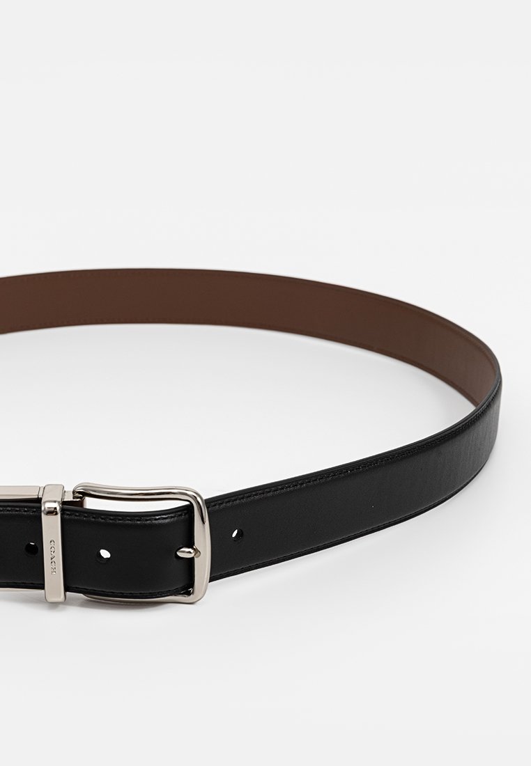 Ceinture en cuir noir avec une finition lisse, boucle en métal argenté et doublure intérieure marron. Elle dispose de plusieurs trous d'ajustement pour s'adapter à différentes tailles.