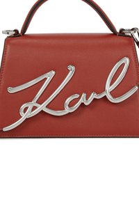 Borsa a mano rossa in pelle con logo in metallo argentato sulla parte anteriore, dalla forma strutturata e con manico superiore. Texture liscia, design minimalista.