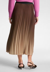 Gonna midi plissettata in tonalità di marrone sfumate, dotata di una cintura elastica nera. Il materiale è leggero con una texture fluida.