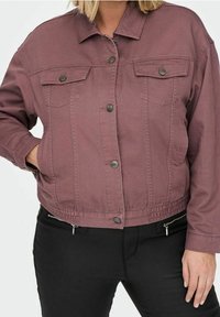 Chaqueta de mezclilla morada con cierre de botones en la parte delantera, dos bolsillos en el pecho y bajo elástico. Presenta detalles de botones plateados y un ajuste holgado.