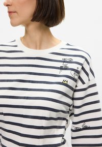 Μακρυμάνικο πουκάμισο με ρίγες σε λευκό και ναυτικό, διαθέτει γραφικά  κεντημένα σχέδια στο στήθος και στο μανίκι. Μαλακό βαμβακερό ύφασμα με άνετη εφαρμογή.