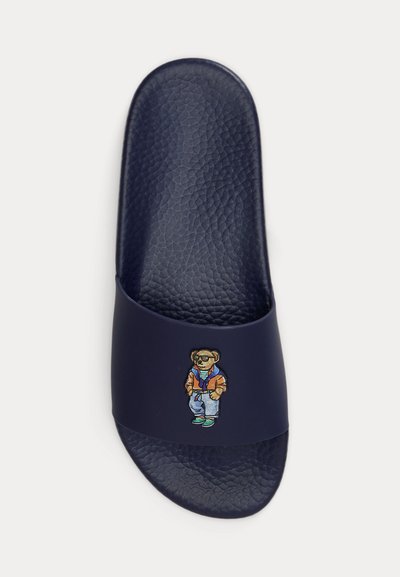 Σαγιονάρα σε ναυτικό μπλε με υφή στο πέλμα και εικονογράφηση ενός αρκούδου που φοράει καθημερινά ρούχα στο λουράκι.