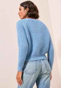 Ljust blå ribbad stickad tröja med avslappnad passform, med långa ärmar och mjuk textur, kombinerad med högmidjade blå jeans.