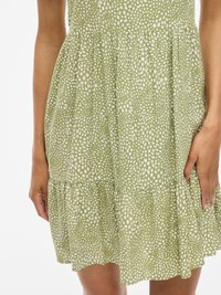 Abito verde con un motivo a macchie bianche, vita arricciata e orlo a balze. Realizzato in tessuto leggero, offre un look casual.
