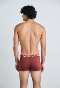 Røde Nike boxerbriefs med en hvit merkebånd i livet, glatt tekstur, tettsittende design og en midt-lår-kutte. Sett bakfra.