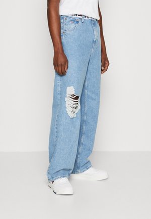 Jeans cu picioare largi de culoare albastru deschis, cu rupturi distresate, având închidere cu nasturi și bucle pentru curea. Combinate cu adidași albi pentru un look casual.
