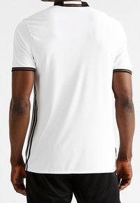 Vit kortärmad sporttröja med svart krage och ärmdekorationer, med svarta sidestreck och en avslappnad passform. Slät tygstruktur.