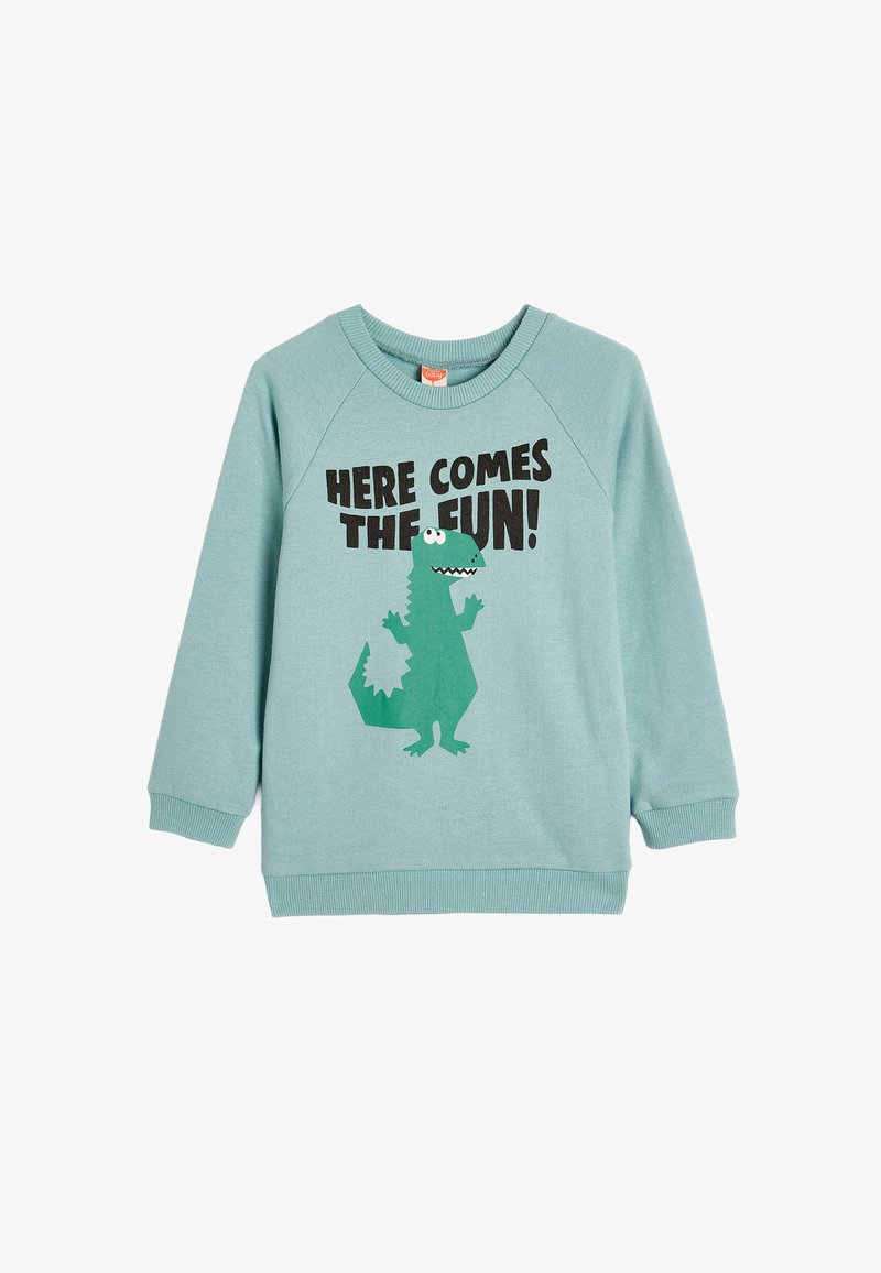 Sudadera de algodón azul claro con mangas raglán, que presenta un gráfico de un dinosaurio verde y un texto negro que dice "¡AQUÍ VIENE LA DIVERSIÓN!"