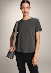 Siv majica s kratkimi rokavi sproščenega kroja, izdelana iz mehke tkanine. V kombinaciji z črnimi leggins in strukturirano sivo torbico.