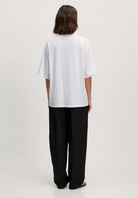 Weißes Baumwoll-T-Shirt mit lockerem Schnitt, überschnittenen Schultern und rundem Halsauschnitt, kombiniert mit schwarzen weiten Hosen. Einfaches Design, glatte Textur.