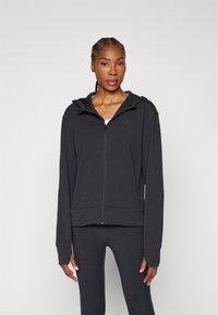 Black zip-up hoodie with a hood, made of soft fabric. Features long sleeves and a fitted waist, minimal branding on the chest.