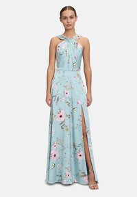 Abito lungo in tessuto azzurro chiaro con motivi floreali, design senza maniche, scollatura plissettata e spacco laterale alta coscia. Tacchi a stiletto argentati.