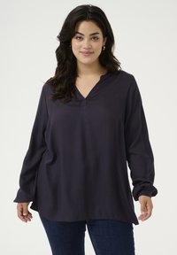 Dark navy long-sleeve top with a v-neckline, relaxed fit, and gathered cuffs. Made of smooth fabric with side slits for ease of movement.