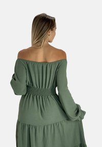 Off-shoulder, langærmet kjole i olivengrøn med elastisk talje og flæset nederdel, lavet af letvægtsstof.