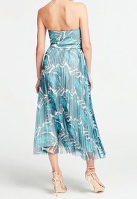 Robe sans bretelles avec une jupe plissée, ornée d'un imprimé floral bleu et blanc. Fabriquée en tissu léger et transparent. Complétée par des talons nus.