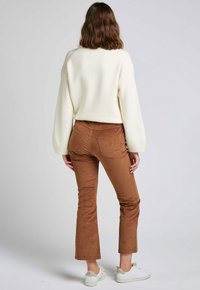 Pull en tricot crème avec une finition texturée, accompagné de pantalons en velours côtelé marron à pattes d'éléphant. Des baskets blanches complètent la tenue.